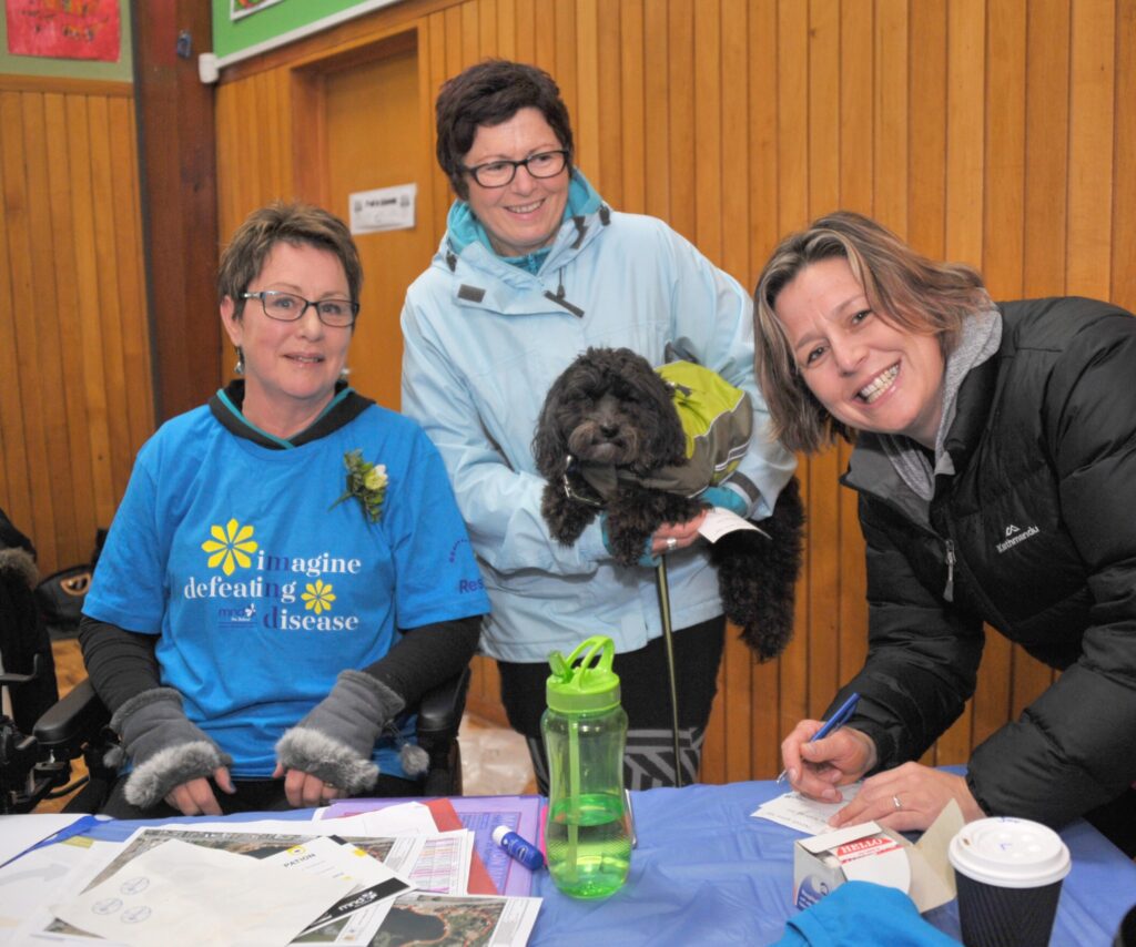 Liz Anderson has Sarah Jones and dog Quigley and Kylie Henricksen of Masterton supporting the cause at the MND charity auction and walk at Lakeview School on Sunday. Pooches were popular on the walk with dozens turning up for the stroll around Henley Lake.