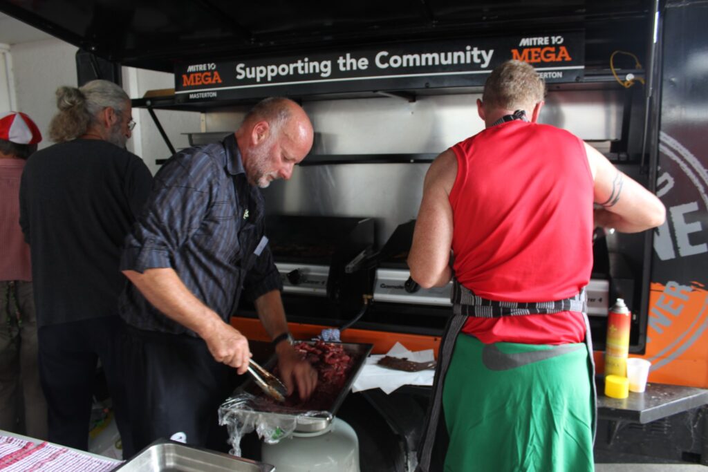 Volunteers cook some Christmas meats on the barbecue supplied by Mitre 10 Mega. PHOTO/EMILY NORMAN